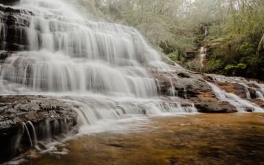 Tiers of cascading mountain water over rocks into a shallow pool