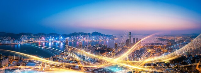 Nighttime aerial view of a city skyline with illuminated skyscrapers and streaking light trails.