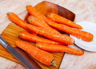 Bunch of fresh orange carrots on wooden cutting board. Preparing food.