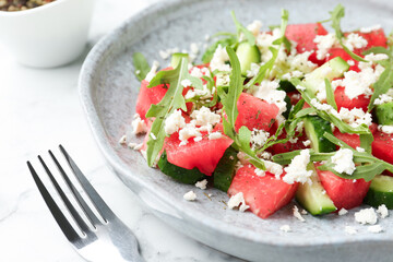 Delicious watermelon salad with feta cheese, cucumber and arugula served on white marble table, closeup
