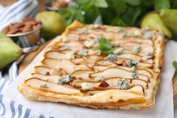 Delicious puff pastry tart with pears, almond, mint and blue cheese on table, closeup