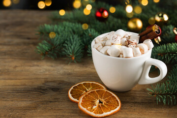 Tasty hot cocoa drink with marshmallows, cinnamon stick in cup and dry orange slices on wooden table, closeup. Space for text