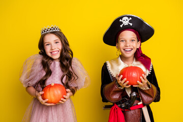 Portrait of two kids halloween princess pirate costume hold pumpkin isolated on yellow color background
