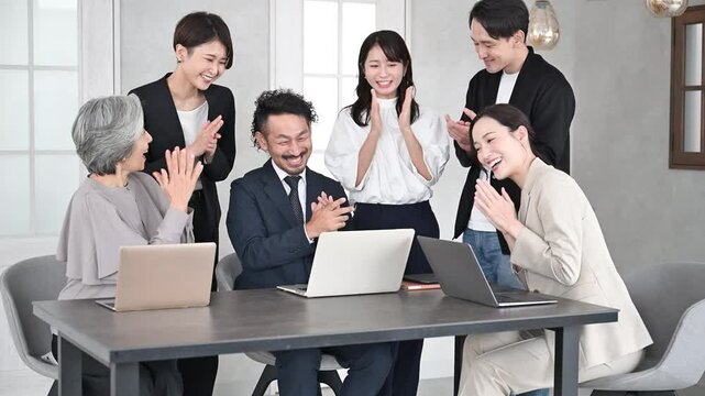 パソコンを見てチームで仕事をする男女の複数のビジネスマンたち　拍手して成功や売上アップなどポシティブに喜ぶイメージの動画