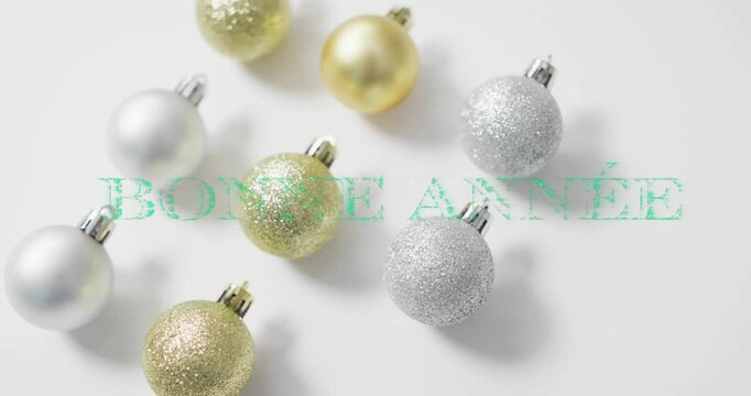 Animation of bonne annee text over christmas baubles on white background