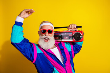 Photo banner of sportive cheerful old man listen music boom box dressed stylish retro sportswear isolated on yellow color background © deagreez