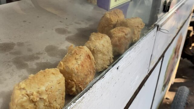 A street vendor carefully arranges crispy tofu in a glass display case, showcasing the freshly fried snacks for customers. The video highlights the preparation and presentation of street food, perfect