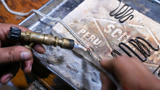 Goldsmith carefully welding a silver chain link using a blowtorch