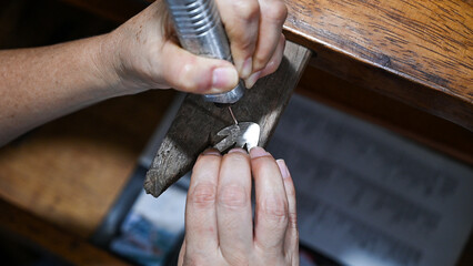 Goldsmith is engraving a silver plate with an electric tool on a wooden table