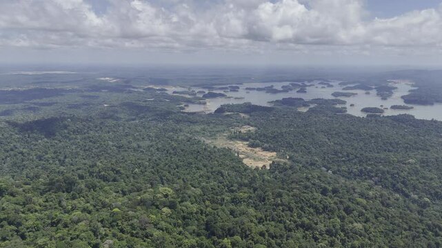 Drone flies from Brownsberg Hill toward valley with forested islands in lake and gold mines along the way in Suriname