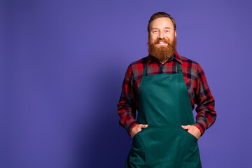 Photo of stylish cheerful man florist wear red plaid shirt green apron standing empty space isolated on purple color background