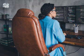 Photo of pretty young girl sit armchair back view coding monitors wear blue shirt coworking programmer successful nice light office