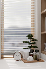 A white table by the window featuring an alarm clock, a decorative plant, and a coffee set on a tray