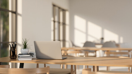 A laptop on a wooden table in a minimalist Scandinavian coffee shop co-working space or library.