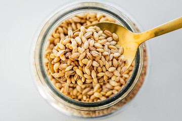 pantry staple close-up, spoonful of barley over clear glass jar shot from above