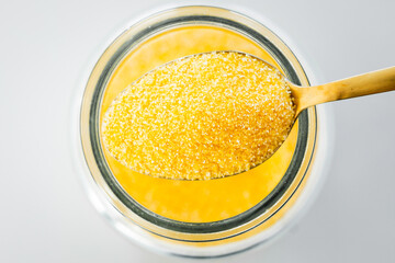 pantry staple close-up, spoonful of instant polenta over clear glass jar shot from above