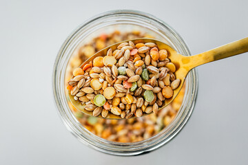 pantry staple close-up, spoonful of dried legume mix over clear glass jar shot from above