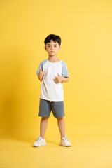 Full body image of asian kid boy wearing summer clothes posing on yellow background