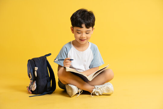 Full body image of a boy holding books, backpack and posing on a yellow background
