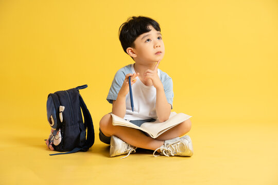 Full body image of a boy holding books, backpack and posing on a yellow background