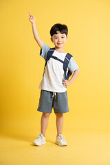 Full body image of an Asian boy wearing a school backpack and posing on a yellow background