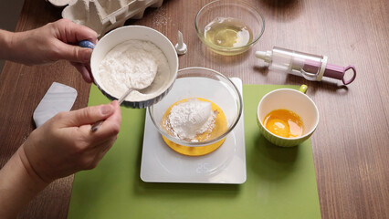 Process of preparing scales and utensils for making dough. Woman weighs flour. Scales, dishes on wooden table. Hands close-up.
