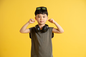 Portrait of an Asian boy wearing a tank top, headphones, and sunglasses posing on a yellow background