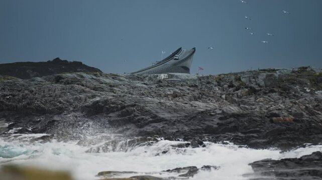 The iconic curve of Storseisundet Bridge rises against a backdrop of rocky coastline and crashing waves.