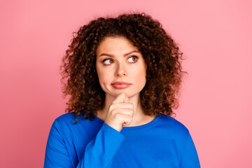 Thoughtful young woman with curly hair contemplating against pink background in casual blue sweatshirt