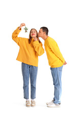 Young couple with mistletoe branch on white background