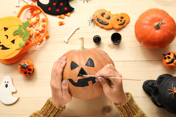 Woman painting Halloween pumpkin at wooden table