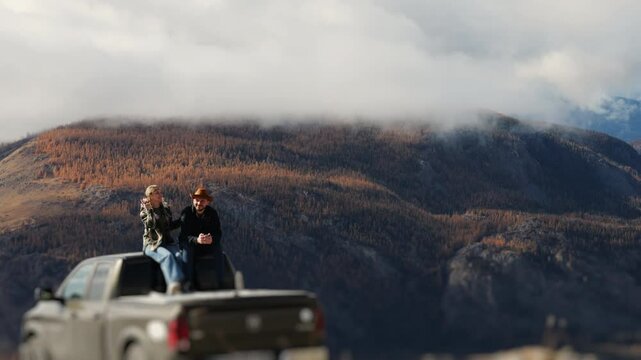 Romantic couple sitting on pickup truck roof enjoying autumn mountain view.
