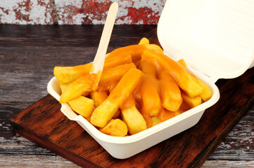 Chips and chip shop curry sauce in a take away box with wooden fork