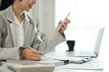 A woman is sitting at a desk with a laptop and a cell phone. She is looking at her cell phone.