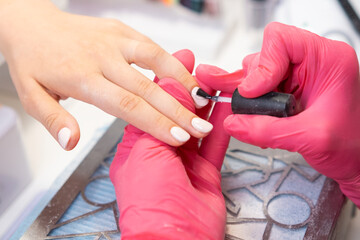 Client receives a top layer of gel polish application on her nude nails while relaxing in a nail salon. 