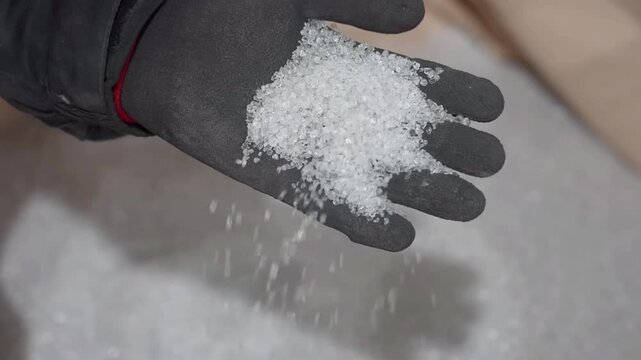 Close up shot, a gloved hand holding a pile of white powder. The powder is falling from the hand onto a surface.