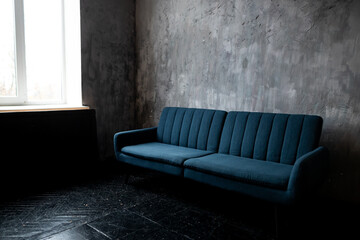 A cozy blue sofa positioned near a window in a minimalist, textured room with gray walls and dark floors, creating a serene atmosphere