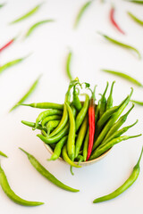A bowl of green and red chilies, surrounded by scattered chilies.