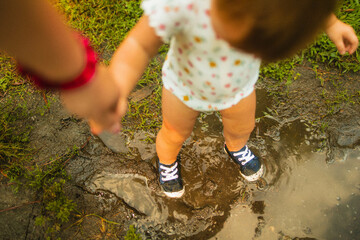 Toddler holding mothers hand while playing in mud puddle