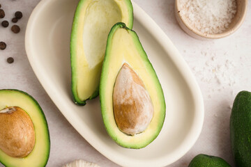 Bowl with halves of fresh ripe avocado and peppercorn on white background