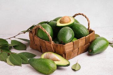 Basket with fresh ripe avocados and leaves on white background