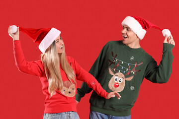 Young couple in Santa hats and Christmas sweaters on red background
