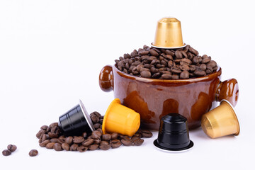 A brown bowl of coffee beans with a capsule on top, surrounded by loose beans and colorful coffee capsules on a bright white background