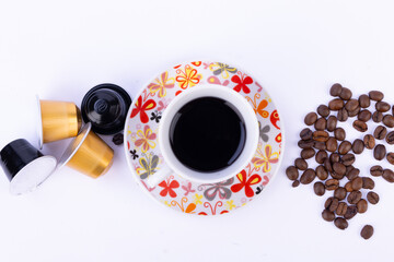 Top view of coffee cup, saucer, beans, and capsules on a clean white background