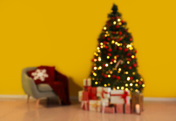 Blurred view of festive living room with Christmas tree, gift boxes, armchair and glowing lights