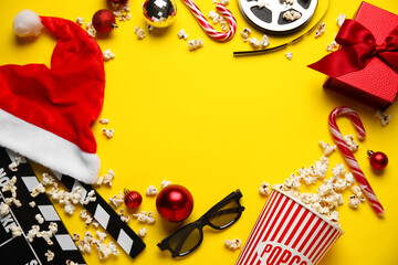 Frame made of bucket of popcorn with 3D glasses, movie clapper and Christmas decor on yellow...