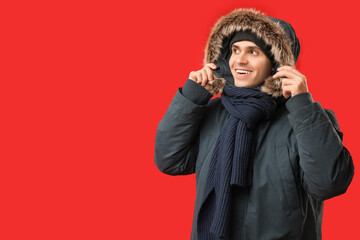 Young man in stylish puffer jacket and scarf on red background