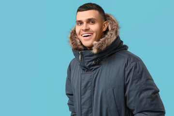 Young man in stylish puffer jacket on blue background