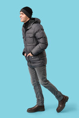 Young man in stylish puffer jacket and hat on blue background