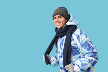 Young man in stylish puffer jacket and scarf on blue background